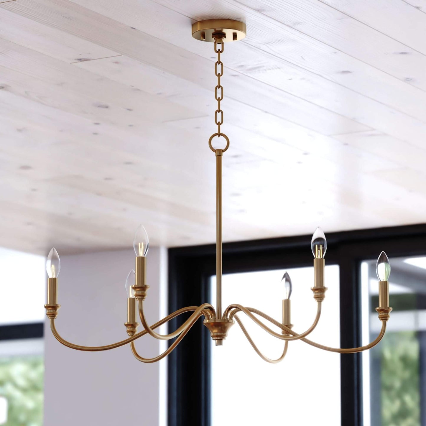 Annabelle 30-inch wide 6-light chandelier in satin brass featuring a steel frame with curved arms, candelabra-style bulbs, round ceiling canopy, and chain suspension, shown installed in a styled interior.