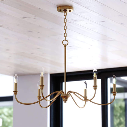 Annabelle 30-inch wide 6-light chandelier in satin brass featuring a steel frame with curved arms, candelabra-style bulbs, round ceiling canopy, and chain suspension, shown installed in a styled interior.
